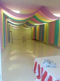 an empty room with rainbow colored curtains on the ceiling and tables in front of it