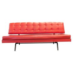 a red leather couch sitting on top of a metal frame bench with black legs and footrests