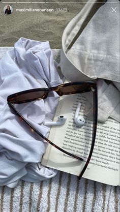 an open book with sunglasses and headphones laying on top of it next to a pair of glasses