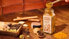 a wooden table topped with lots of different types of spices and seasoning next to a jar filled with cinnamons