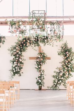 a cross decorated with flowers and greenery in front of a white wall at a wedding