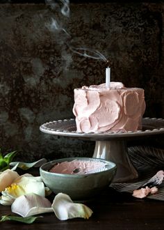 a pink cake sitting on top of a table next to a bowl and plate with flowers