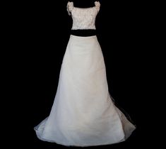 a white wedding dress with black sash on a mannequin headdress in front of a black background