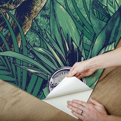 a person is wrapping up a piece of paper on top of a table with a painting behind it