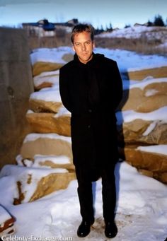 a man standing in the snow wearing a black suit and tie with his hands on his hips