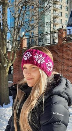 a woman in winter clothing standing next to a tree wearing a headband with flowers on it