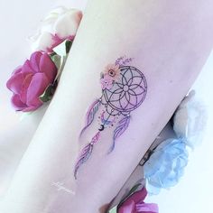 a woman's leg with a watercolor dream catcher tattoo on her left thigh