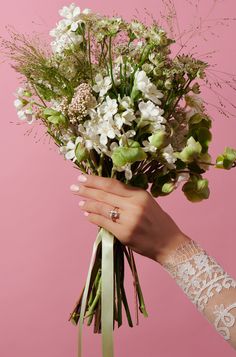 a woman's hand holding a bouquet of flowers against a pink background with lace