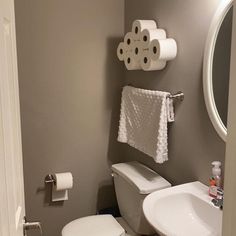 a white toilet sitting next to a sink in a bathroom under a round mirror with two rolls of toilet paper on it