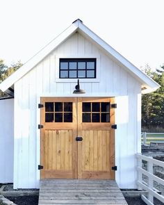 two wooden doors are on the side of a white building with wood steps leading up to it