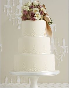 a three tiered white wedding cake with purple and white flowers on the top layer