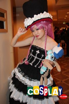 a woman with pink hair wearing a black and white dress holding a stuffed animal in her hand