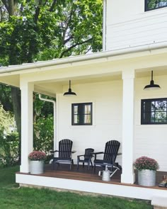 two chairs are on the front porch of a white house with black shutters and windows