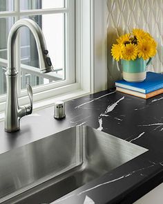 a kitchen sink sitting next to a window with yellow flowers in the vase on it