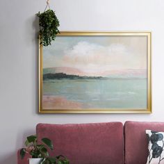 a painting hanging on the wall above a pink couch in a living room with potted plants