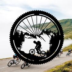 a group of people riding bikes down a road next to a giant wheel with the silhouette of two men on it