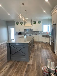 a kitchen with white cabinets and gray island in the middle, surrounded by wood flooring