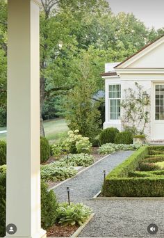 a white house surrounded by trees and bushes in front of it is an entry way that leads to a formal garden area