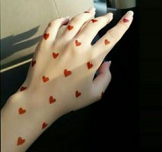 a woman's hand with red hearts painted on her arm and fingers, in front of a car door