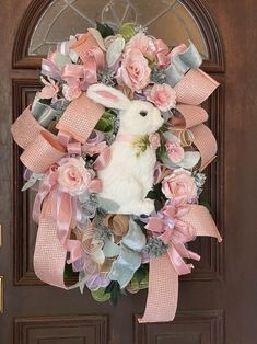 a wreath with pink flowers and a white bunny on it is hanging on the front door