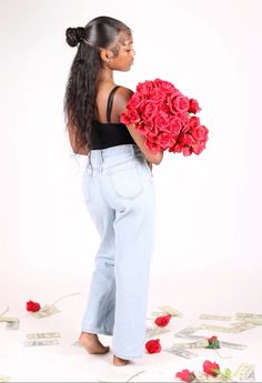 a woman holding flowers in her hands while standing next to money bills and roses on the ground