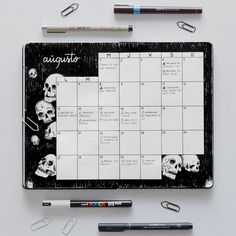 a black and white calendar with skulls on it next to markers, pens and pencils