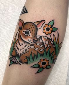 a small deer tattoo on the left arm and calf's head in grass with flowers around it