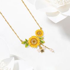 Indulge in the delicate beauty of nature with this stunning Sunflower & Bee Necklace. Crafted from brass and enamel, it features a dainty charm that perfectly captures the essence of the beloved cottagecore aesthetic. A timeless symbol of beauty, it will look simply stunning when worn. This exquisite necklace captures the beauty of summer, featuring a sunflower and a bee crafted from sparkling Selenichast. DETAILS Plating: 18K Gold Materials: 18K Gold on Brass, Enamel, Cubic Zirconia Size:  Leng Dainty Flower-shaped Enamel Jewelry, Yellow Enamel Flower Shaped Jewelry, Yellow Flower-shaped Enamel Jewelry, Sunflower Jewelry, Timeless Symbol, Sunflower Pendant, Sunflower Necklace, Bee Crafts, Bee Necklace