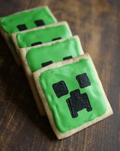 three decorated cookies sitting on top of a wooden table covered in green frosted icing