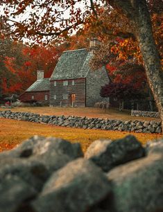 a stone wall and tree in front of a brick house with autumn foliage around it