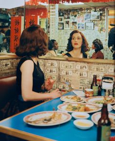 two women sitting at a table with plates of food on it in front of a mirror