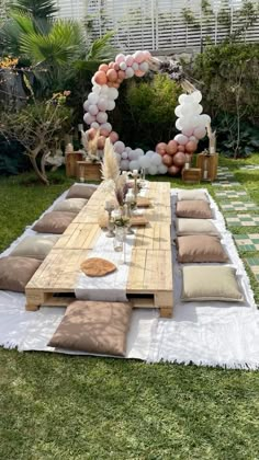 a table with pillows and balloons on it in the middle of a yard area for an outdoor party