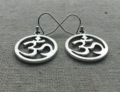 "Stunning silver Ohm round earrings. These are the perfect accessory for any yoga, meditation lover. Bring a little namaste into your life. Made from allergy free plated silver. They measure 5/8\" across by 3/4\" long and hang from simple silver ear wire hooks. I have a matching necklace in my Etsy shop. Here is the link https://etsy.me/2VBdAv9 Thanks for stopping by! Please take a moment and visit the rest of my Etsy shop. I have many more unique and stylish jewelry to choose from. 🌸 Tiger Flo Symbolic Round Earrings For Pierced Ears, Symbolic Round Metal Earrings, Nickel-free Symbolic Round Earrings, Symbolic Nickel-free Round Earrings, Symbolic Round Nickel-free Earrings, Symbolic Round Pierced Earrings, Pierced Symbolic Round Earrings, Ohm Jewelry, Om Earrings