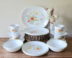 a table topped with lots of white plates and bowls next to a vase filled with flowers