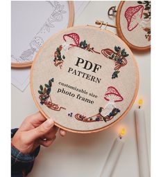 a person holding up a cross stitch pattern in front of two embroidery hoops with the words pdf on them