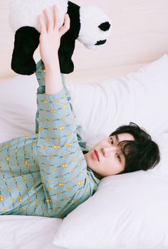 a young boy laying on top of a bed holding a stuffed animal above his head