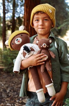 a young boy holding two teddy bears in the woods