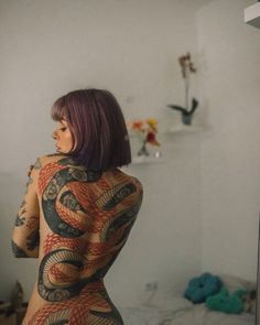 a woman with tattoos on her body standing in front of a mirror