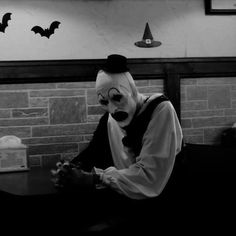 a man dressed as a clown sitting at a table in front of a brick wall