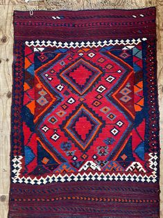 an old red and blue rug on wooden floor with wood planks in the background