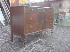 an old wooden dresser sitting in the middle of a dirt floored area next to a building