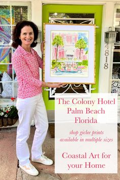 a woman standing in front of a green door holding up a framed art piece that says the colony hotel palm beach florida