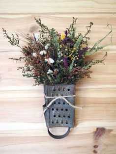 a metal grater with flowers tied to it on a wooden wall next to a planter