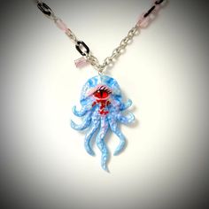 Introducing our Handcrafted Octopus Polymer Clay Necklace, a truly exceptional piece of wearable art. This necklace features a striking octopus pendant with a one-of-a-kind red cat-eye design meticulously handcrafted from polymer clay. The vivid red hues accentuate the octopus's captivating charm, while the delicate light blue color of the octopus itself adds a touch of whimsy. Suspended elegantly from a silver chain, this necklace offers both charm and versatility. Whether you're celebrating the enchantment of Halloween, the romance of Valentine's Day, the milestone of an anniversary, or the joy of a birthday, this necklace is a perfect choice. The octopus, known for its intelligence and mystery, adds a touch of intrigue to your style. This necklace is more than just jewelry; it's a conve Handmade Novelty Resin Jewelry, Blue Enamel Necklaces With Lobster Clasp, Handmade Blue Wearable Art Necklace, Whimsical Blue Pendant Jewelry, Handmade Blue Necklace In Wearable Art Style, Handmade Themed Pendant Jewelry, Blue Wearable Art Necklace As Gift, Blue Wearable Art Necklace For Gift, Hand Painted Blue Wearable Art Jewelry