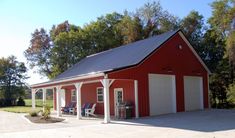 a red and white barn with two chairs on the porch next to it, surrounded by trees