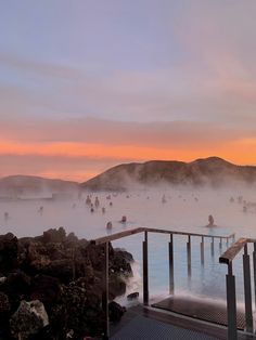 people are in the water at sunset with steam rising up from the ground and hills behind them