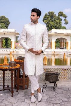 Item Contains:  Sherwani Kruta  Pyjama & Shoes  Fabrics :   Silk  Colours :  Ivory Style and Designs :  Sherwani has mandarin collar and long sleeves with a full button placket symmetric hem and multiple slits it has all over checked thread and mirror work Kurta has mandarin collar and long sleeves with a full button placket symmetric hem and multiple slits Slim fit Traditional Churidar Pants Made of Raw Silk Nara Clousure Style  Size :  Slim fit  Model height is 6 fitt and wearing 40 size  Mate White Sherwani For Men Wedding, White Semi-stitched Sherwani For Festivals, Festival White Semi-stitched Sherwani, White Sherwani For Groom For Eid, White Traditional Wear With Resham Embroidery For Groom, White Dabka Sherwani For Groom, White Resham Embroidery Traditional Wear For Groom, White Naqshi Churidar For Festivals, White Traditional Wear For Groom At Festivals