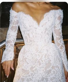 a woman wearing a white lace dress with long sleeves and an open back is posing for the camera