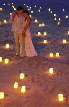 a man and woman standing in the sand surrounded by lit candles