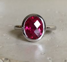 "A Classic oval shaped Faceted Lab Created Ruby Sterling Silver Ring featuring a comfort fit band with a bezel around the stone. This makes a great birthstone ring for those July Birthdays! Wrapped in a box ready for gift giving.(r-537) RING INFO ---------------- STERLING SILVER Stone with Bezel measure 11.5mm x 10mm July BIRTHSTONE *Follow us @belesasjewelry on Instagram for promotions/giveaways *LIKE* us on Facebook http://www.facebook.com/Belesas *If you like the ring, please click on the \"P Red Ruby Ring With Bezel Setting, Adjustable Oval Red Ruby Ring, Adjustable Red Oval Ruby Ring, Modern Oval Ruby Ring With Bezel Setting, Red Oval Ring With Bezel Setting, Red Oval Rings With Bezel Setting, Red Oval Stackable Promise Rings, Red Gemstone Ring, Red Ring